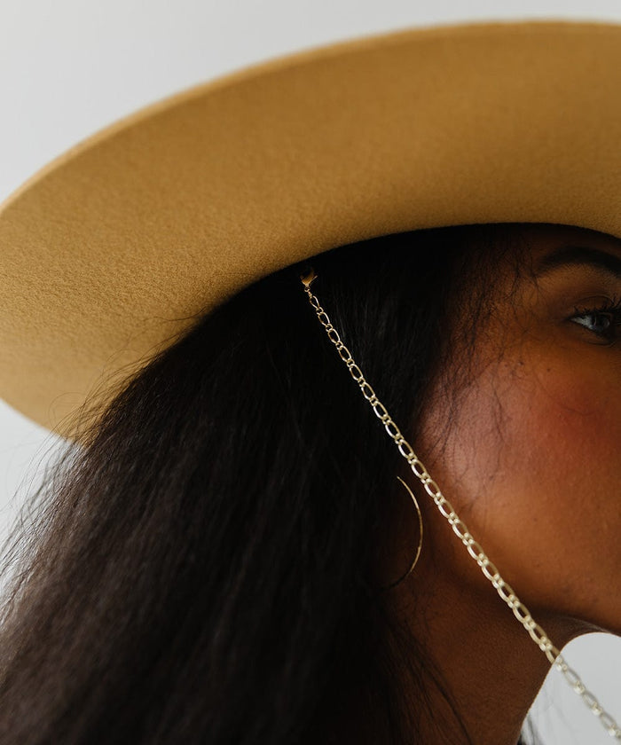 Close up image of a woman wearing a wide brim hat with a chain against a plain background #color_honeycomb