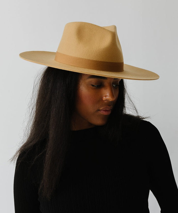 Woman wearing a honeycomb  colored wide brim fedora hat with a band and a black t-shirt, looking sideways against a plain background #color_honeycomb