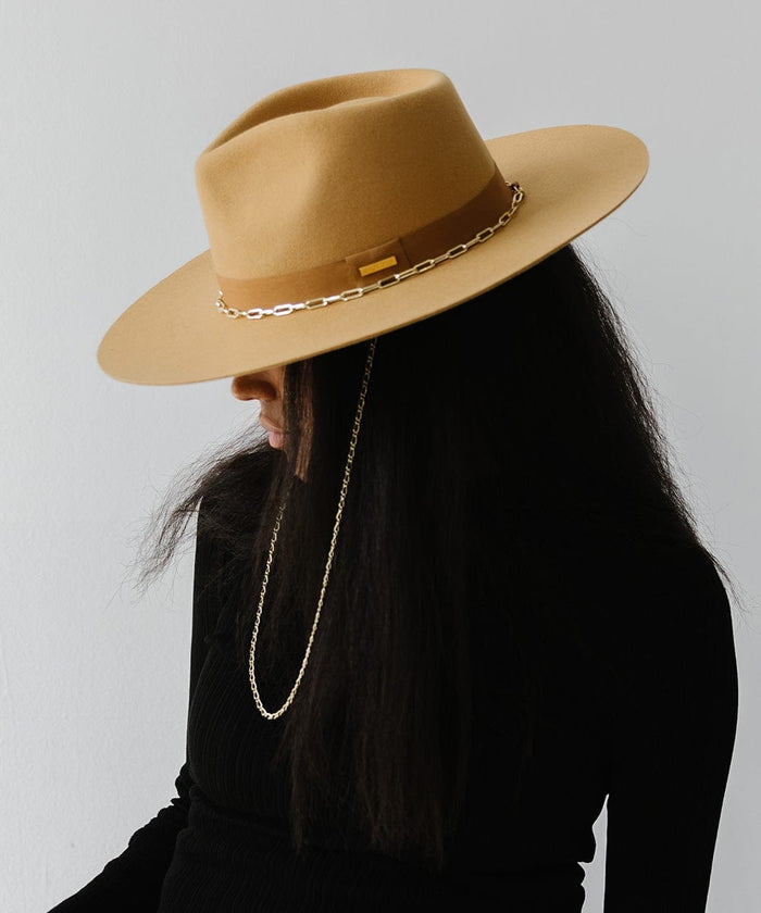 Person wearing a honeycomb  colored wide brim fedora hat with a band and a gold chain detail around the base of the crown and a black t-shirt, posing against a plain background #color_honeycomb