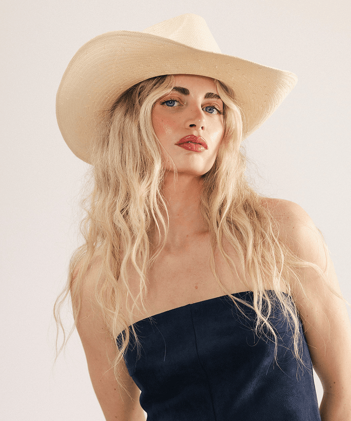 Woman wearing a natural colored straw cowboy hat with a fedora crown and a rolled western brim, displayed on a white background. #color_natural