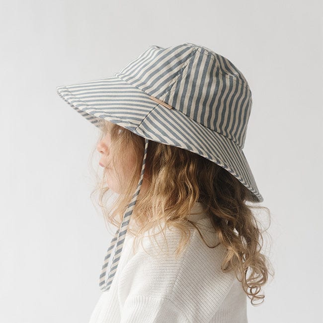 Young girl wearing a blue and white striped bucket hat and a white shirt, facing sideways against a plain background #color_striped - blue