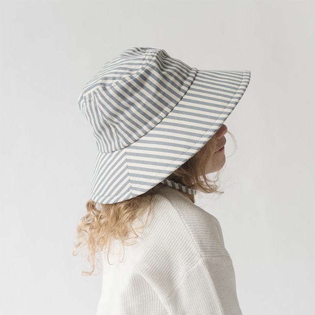 Young girl wearing a blue and white striped bucket hat and a white shirt, posing sideways against a plain background #color_striped - blue