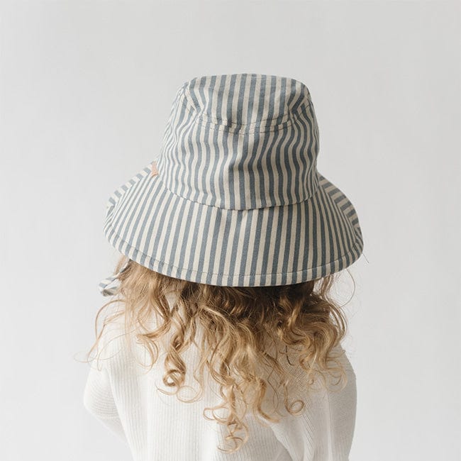Young girl wearing a blue and white striped bucket hat and a white shirt, facing behind against a plain background #color_striped - blue