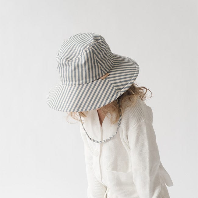 Young girl wearing a blue and white striped bucket hat and a white shirt, looking down against a plain background #color_striped - blue