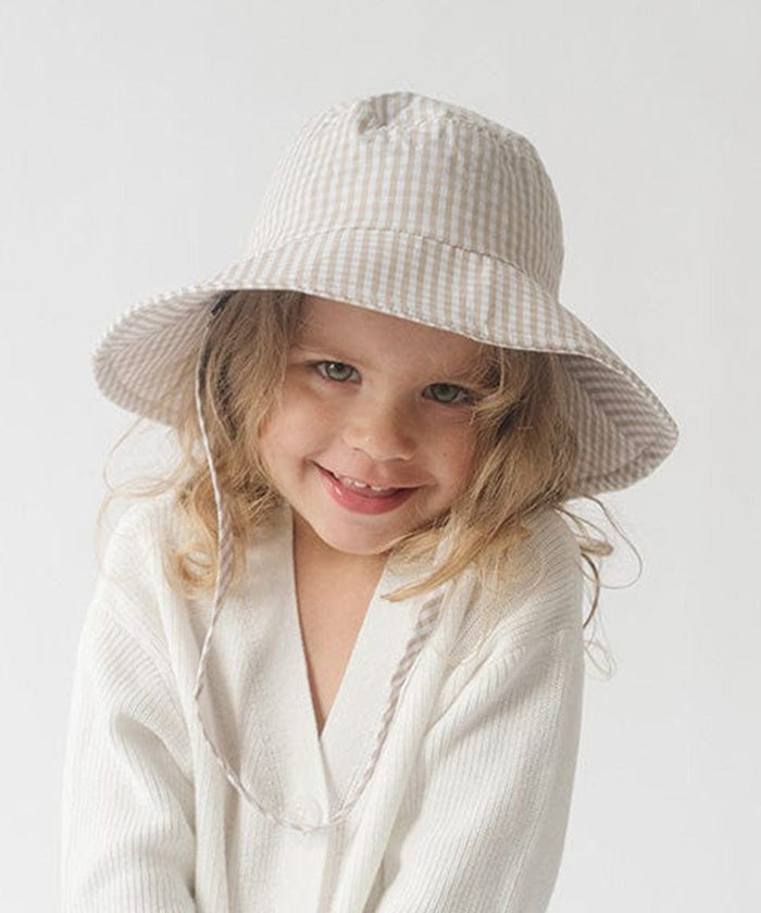 Young girl wearing a latte colored bucket hat and a white shirt against a plain background #color_latte