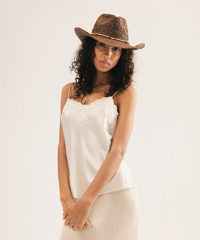 Woman wearing a white lace top and straw hat against a white background #color_chocolate