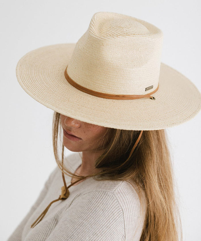 Woman wearing an ivory palm straw sun hat with a brown chinstrap and a white t-shirt, looking sideways against a plain background #color_ivory