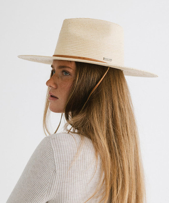 Woman with long hair wearing an ivory palm straw sun hat with a brown chinstrap and a white t-shirt, facing sideways against a plain background #color_ivory