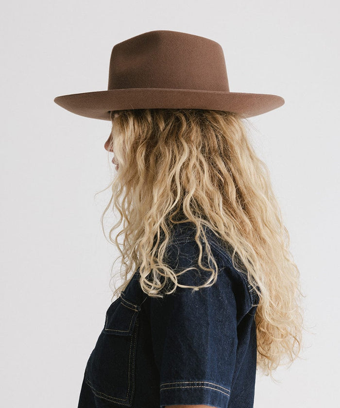 Woman wearing a chocolate colored Rowan Wide Brim Fedora Hat and a denim shirt, facing sideways against a plain background #color_chocolate