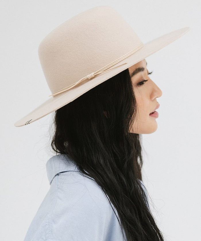 Woman wearing a cream open crown hat with a hat band and a blue shirt, facing sideways against a plain background  #color_cream