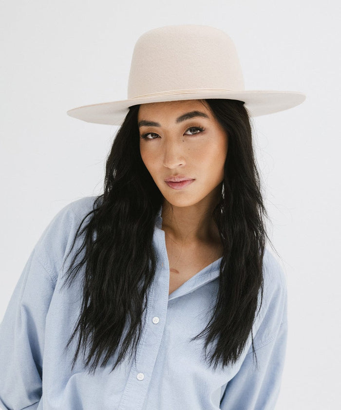 Woman wearing a cream open crown hat with a hat band and a blue shirt, posing against a plain background  #color_cream