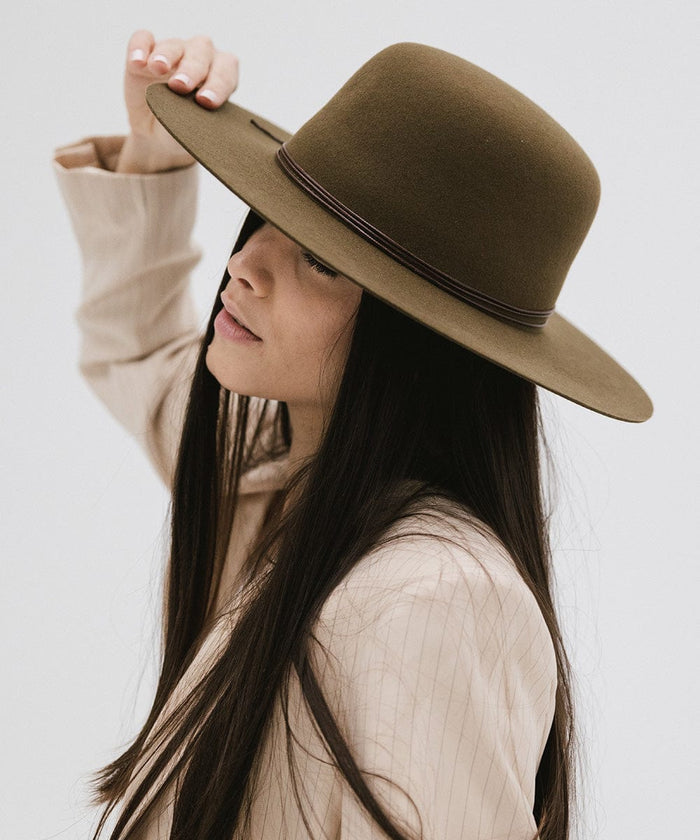 Woman wearing an olive colored open crown hat with a hat band and a cream blazer, posing sideways  against a plain background #color_olive