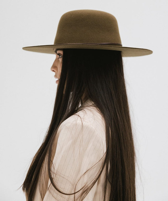Woman wearing an olive colored open crown hat with a hat band and a cream blazer, facing sideways  against a plain background #color_olive