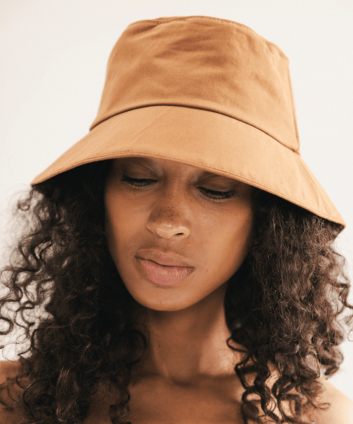 Woman wearing a brown bucket hat with a plain background #color_brown