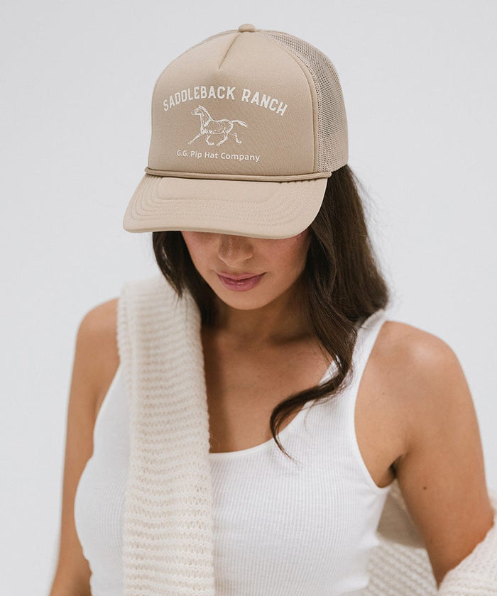 Woman wearing a tan cap with 'Saddleback Ranch' text and logo, and a white top, posing against a plain background  #color_tan