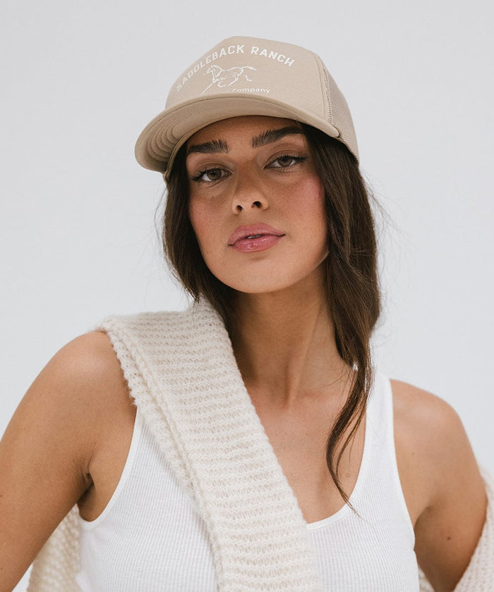 Woman wearing a tan cap with 'Saddleback Ranch' text and logo, and a white top against a plain background  #color_tan