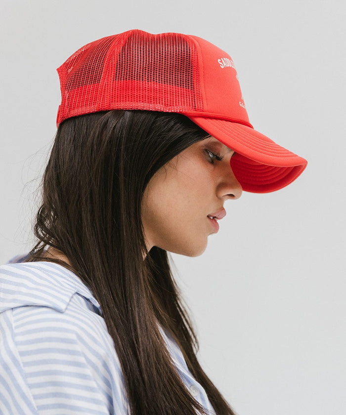 Woman wearing a vintage red colored cap with 'Saddleback Ranch' text and logo, and a light colored shirt, facing sideways against a plain background  #color_vintage red