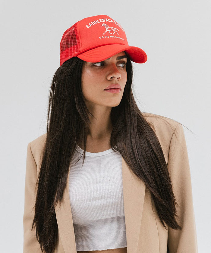 Woman wearing a vintage red colored cap with 'Saddleback Ranch' text and logo, a white top and beige coat against a plain background  #color_vintage red