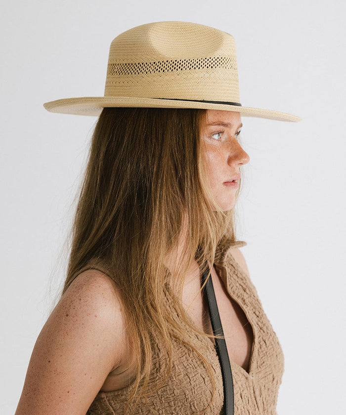 Woman wearing a natural colored straw fedora hat with a hat band and a brown top, facing sideways against a plain background #color_natural