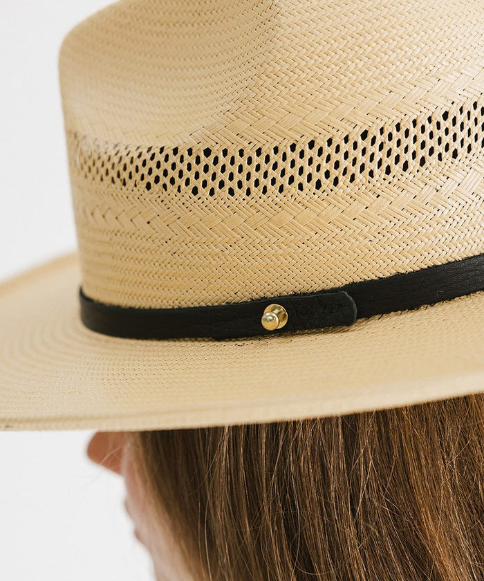 Close up image of a person wearing a natural colored straw fedora hat with a hat band against a plain background #color_natural