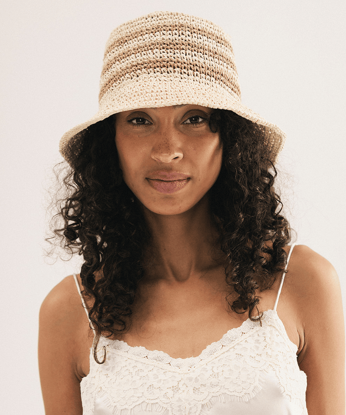Woman wearing a straw bucket hat against a plain background #color_natural stripe