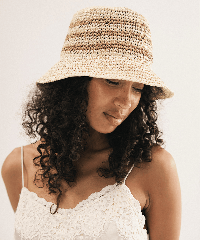 Woman wearing a straw bucket hat against a plain background #color_natural stripe