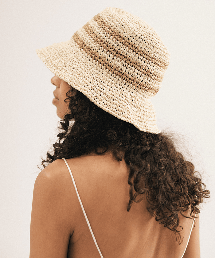Woman wearing a straw bucket hat against a plain background #color_natural stripe