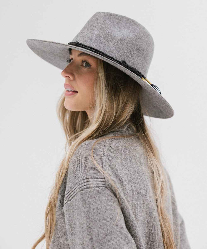 Woman wearing a grey wide brim fedora hat with a hat band and a grey sweater, looking sideways against a plain background #color_grey