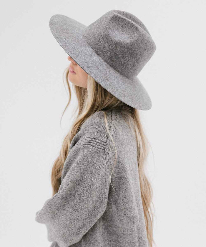 Woman wearing a grey wide brim fedora hat and a grey sweater, facing sideways against a plain background #color_grey