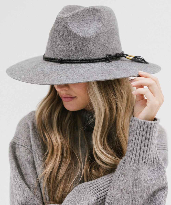 Woman wearing a grey wide brim fedora hat with a hat band and a grey sweater, posing against a plain background #color_grey