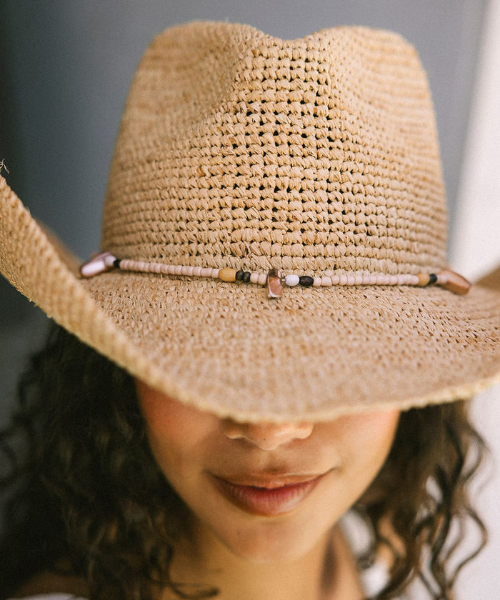 Close-up of a woman wearing a straw hat with a beaded band against a neutral background #color_natural