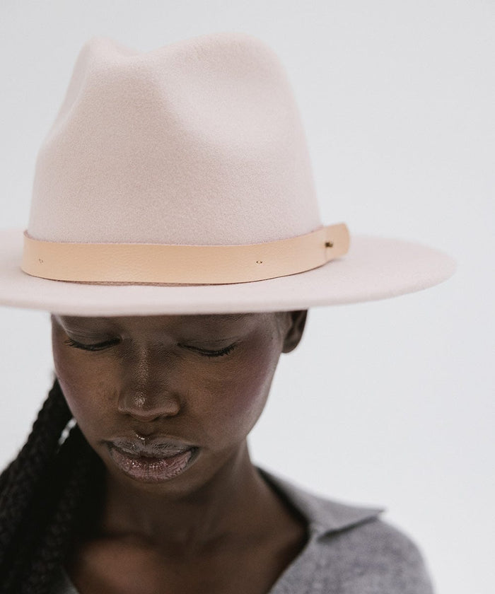 Close up image of a woman wearing a blush pink colored fedora hat with a hat band against a plain background  #color_blush pink