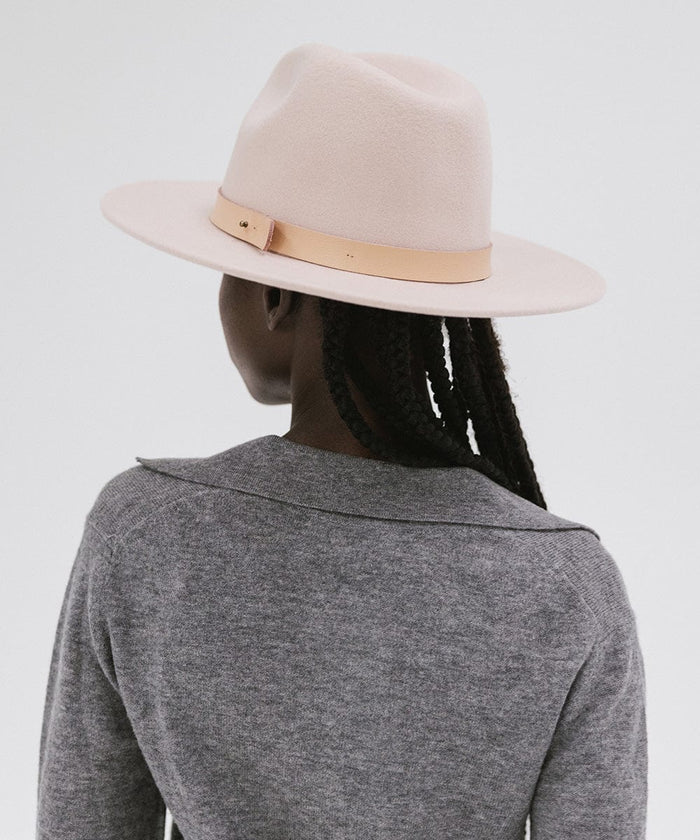 Person wearing a blush pink colored fedora hat with a hat band and a grey shirt, facing behind against a plain background  #color_blush pink
