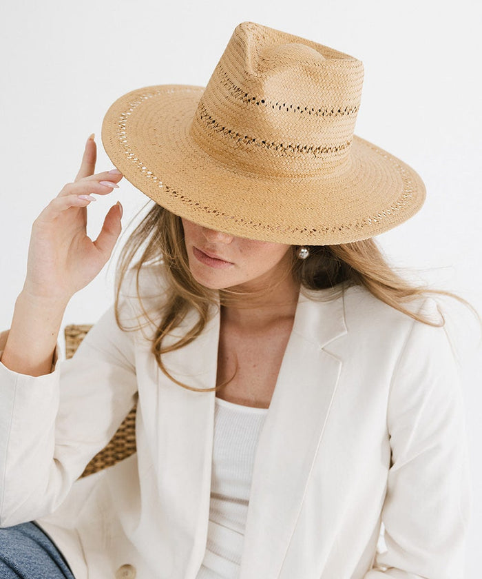 Woman wearing a honey colored teardrop straw fedora hat and a white top with a white blazer, posing against a plain background #color_honey