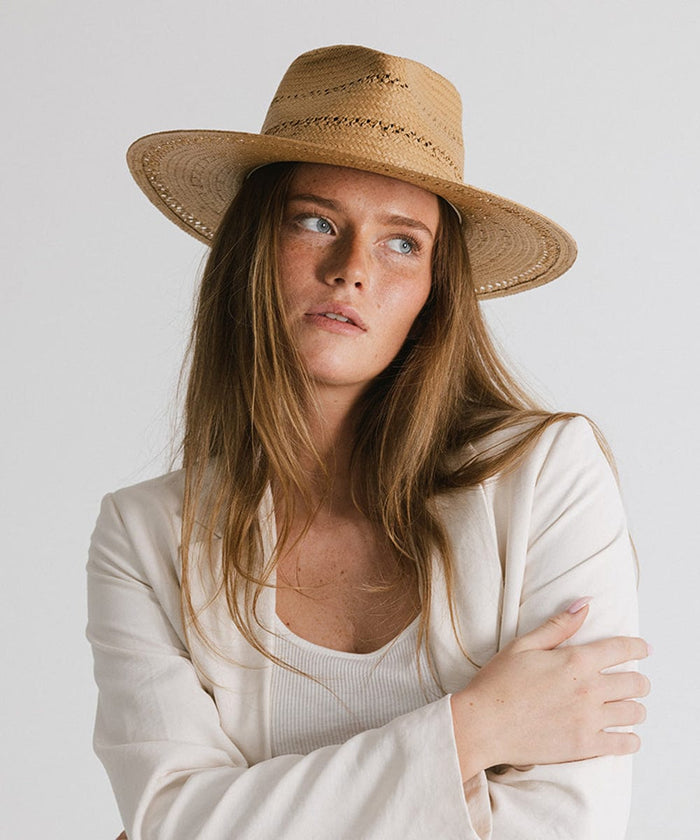 Woman wearing a honey colored teardrop straw fedora hat and a white blazer, looking sideways against a plain background #color_honey