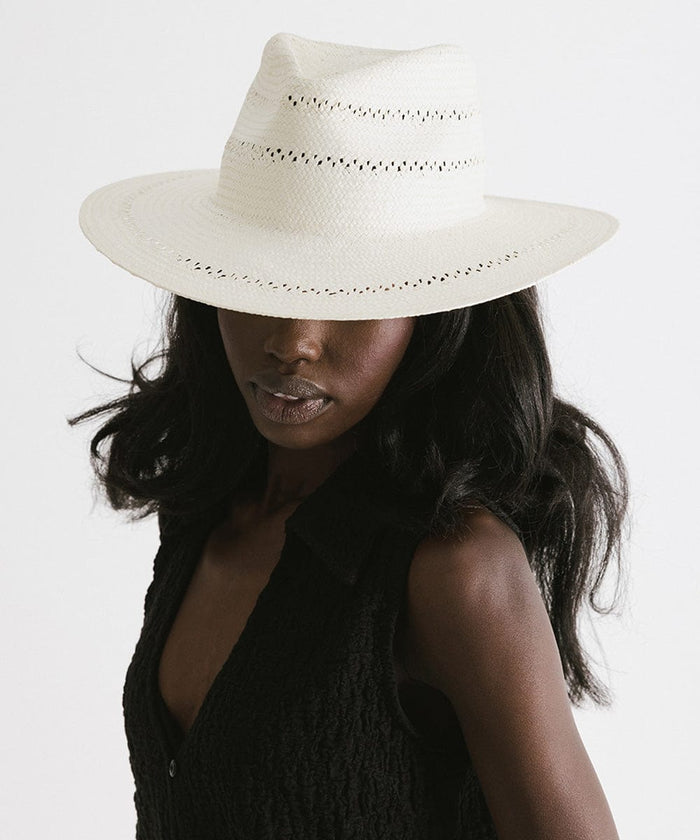 Woman wearing a white straw fedora hat with decorative trim and a black top against a plain background  #color_white
