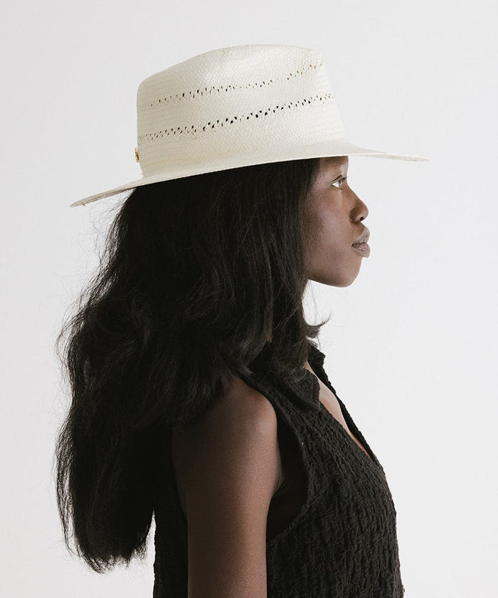 Woman wearing a white straw fedora hat with decorative trim and a black top, facing sideways against a plain background  #color_white