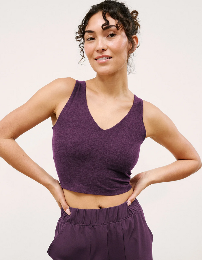 Woman wearing a blackberry-colored tank top and high-waisted pants against a light background