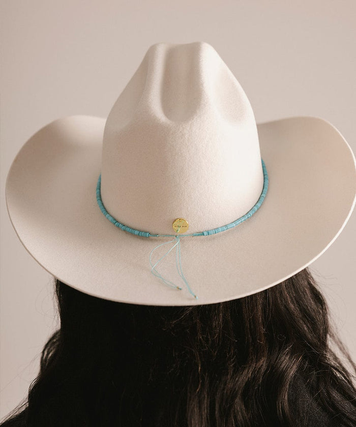 White cowboy hat with a blue band worn by a person against a neutral background #color_turquoise