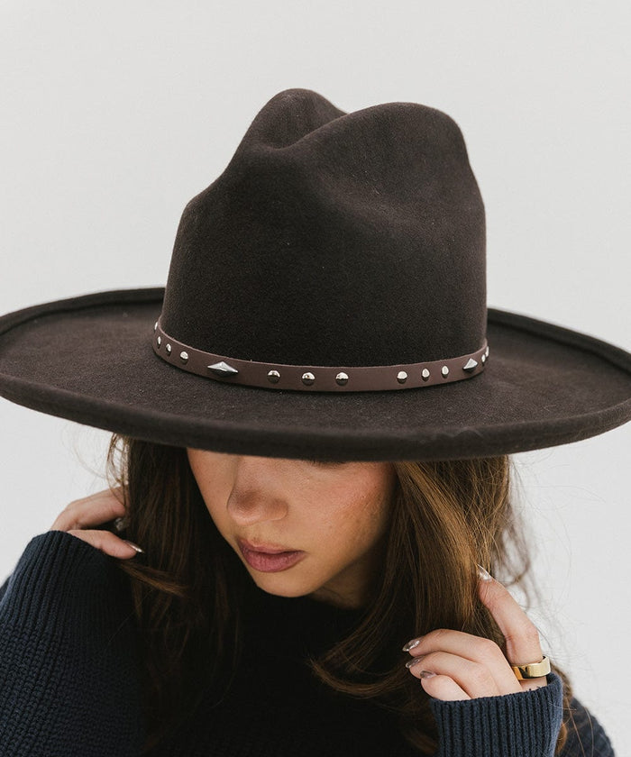 Woman wearing a brown hat with a chocolate colored studded leather hat band against a plain background #color_chocolate