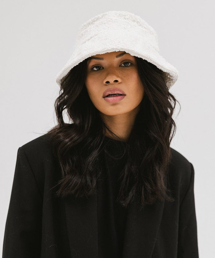 Woman wearing a white bucket hat and a black t-shirt with a black blazer against a plain background  #color_white