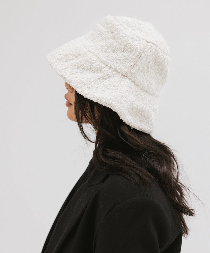 Woman wearing a white bucket hat and a black blazer, facing sideways against a plain background  #color_white
