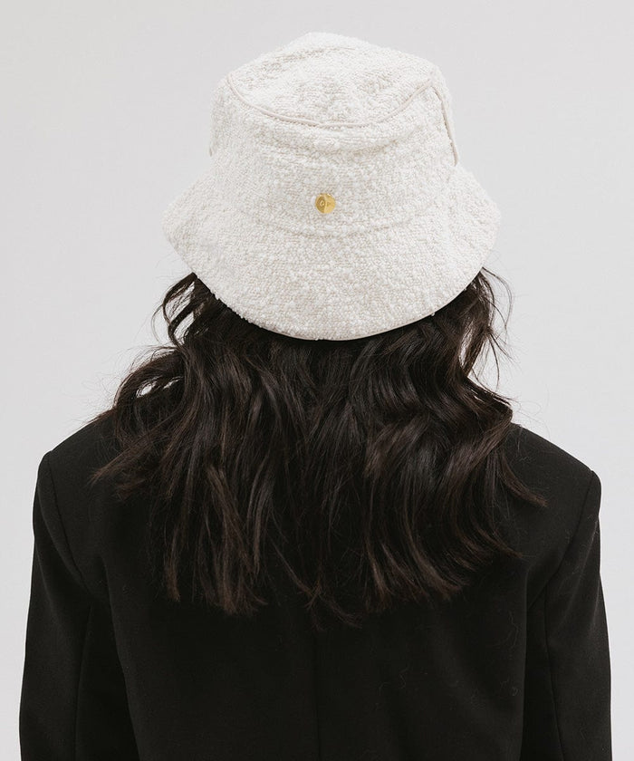 Woman wearing a white bucket hat and a black blazer, facing behind against a plain background  #color_white