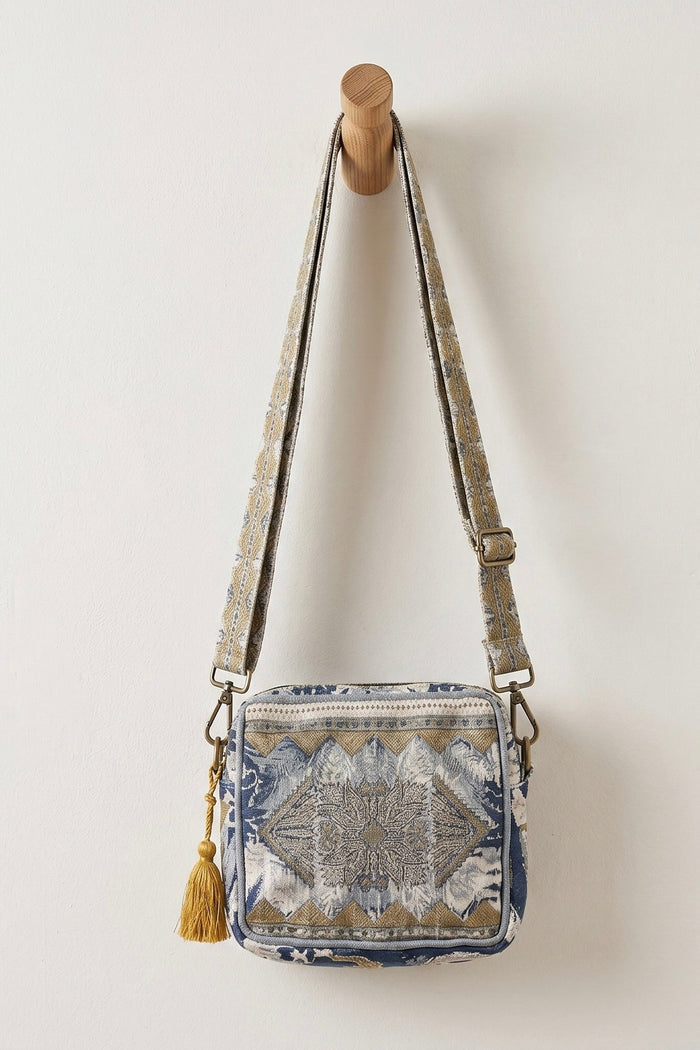 Blue and tan woven tapestry crossbody bag with geometric pattern, adjustable strap, zip-top closure, and tassel charm for boho western style.