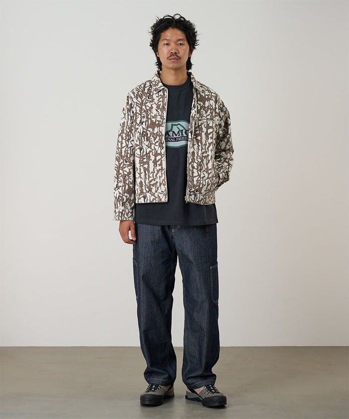 Model wearing a moss green Gramicci Taos Canvas Jacket and blue jeans on a light-tone background.