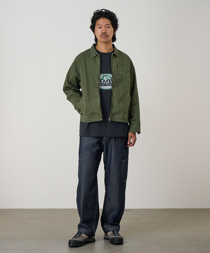 Model wearing a moss green Gramicci Taos Canvas Jacket and blue jeans on a light-tone background.