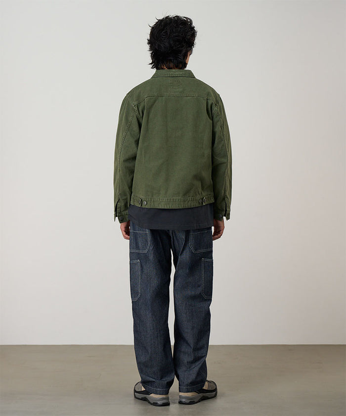 Back view of a model wearing a moss green Gramicci Taos Canvas Jacket and blue jeans on a light-tone background.