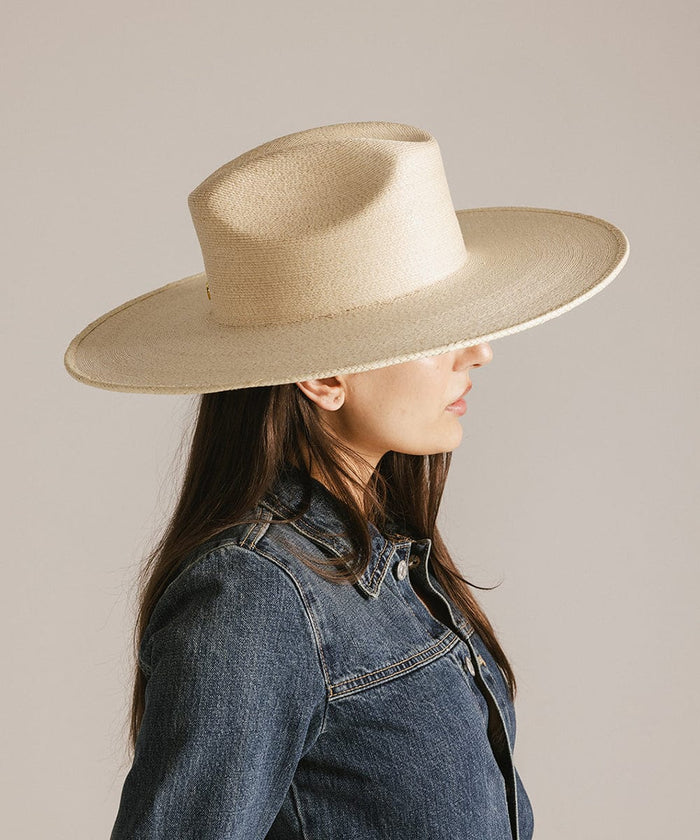 Woman wearing a natural colored western wide brim straw hat and a denim jacket, facing sideways against a plain background #color_natural