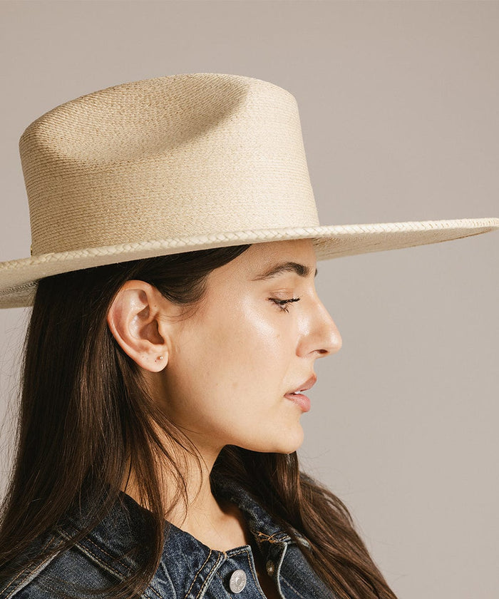 Woman wearing a natural colored western wide brim straw hat, facing sideways against a plain background #color_natural