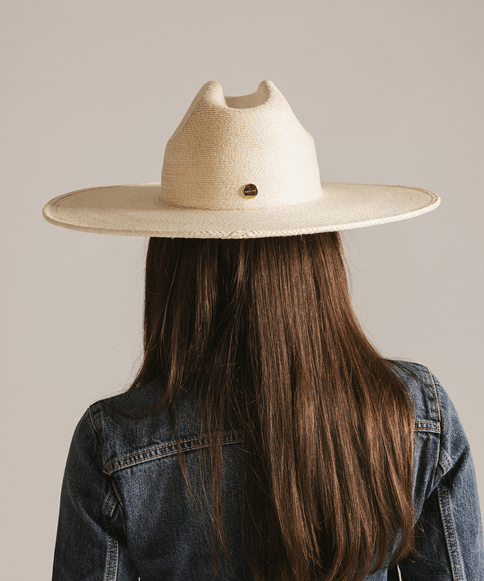 Person with long hair wearing a natural colored western wide brim straw hat and a denim jacket against a plain background #color_natural